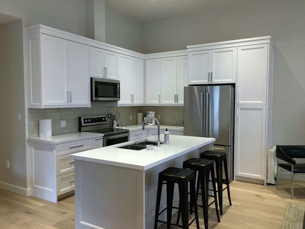 Compact white shaker kitchen with a quartz island, seating for three and a full-height pantry wall around the fridge