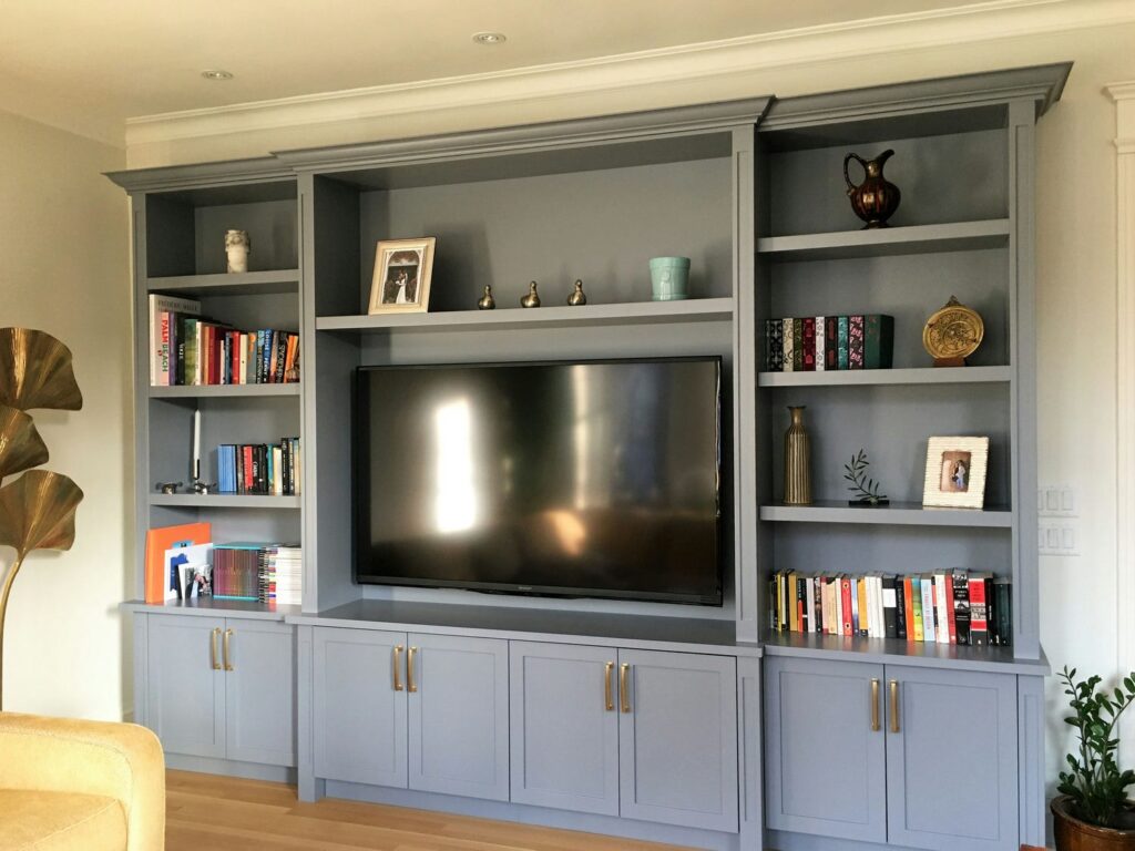 Blue grey custom TV wall unit with bridged bookcases, adjustable shelving and closed base storage with brass pulls