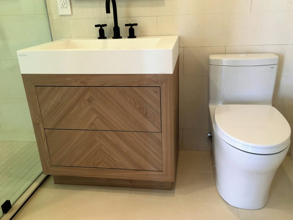 White oak vanity with herringbone veneer drawer fronts, an integrated white sink top and a matte black cross-handle faucet