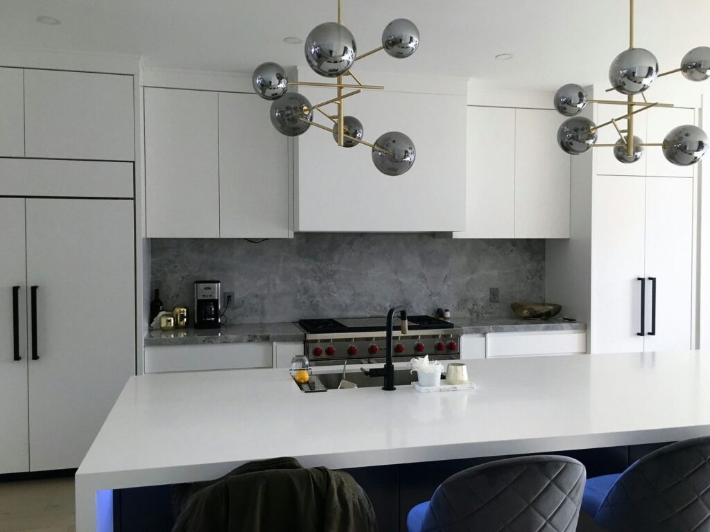 Handleless white modern kitchen with grey stone slab backsplash, professional rangetop and a navy island with white waterfall top