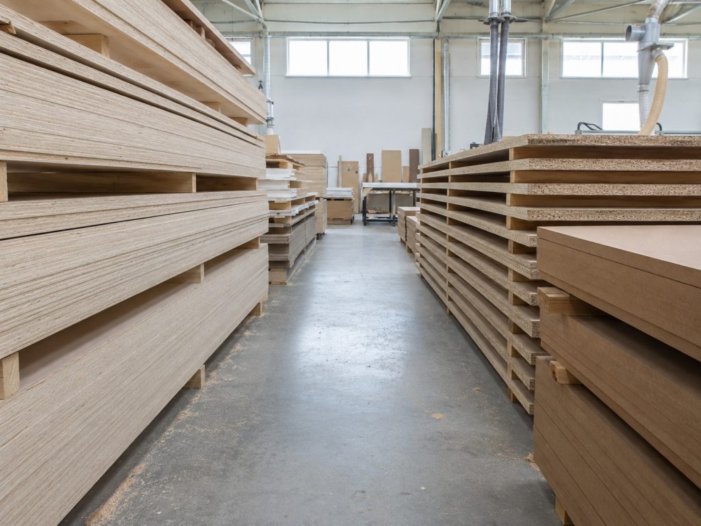 Full sheets of plywood, particleboard, and MDF stacked in a custom cabinet workshop